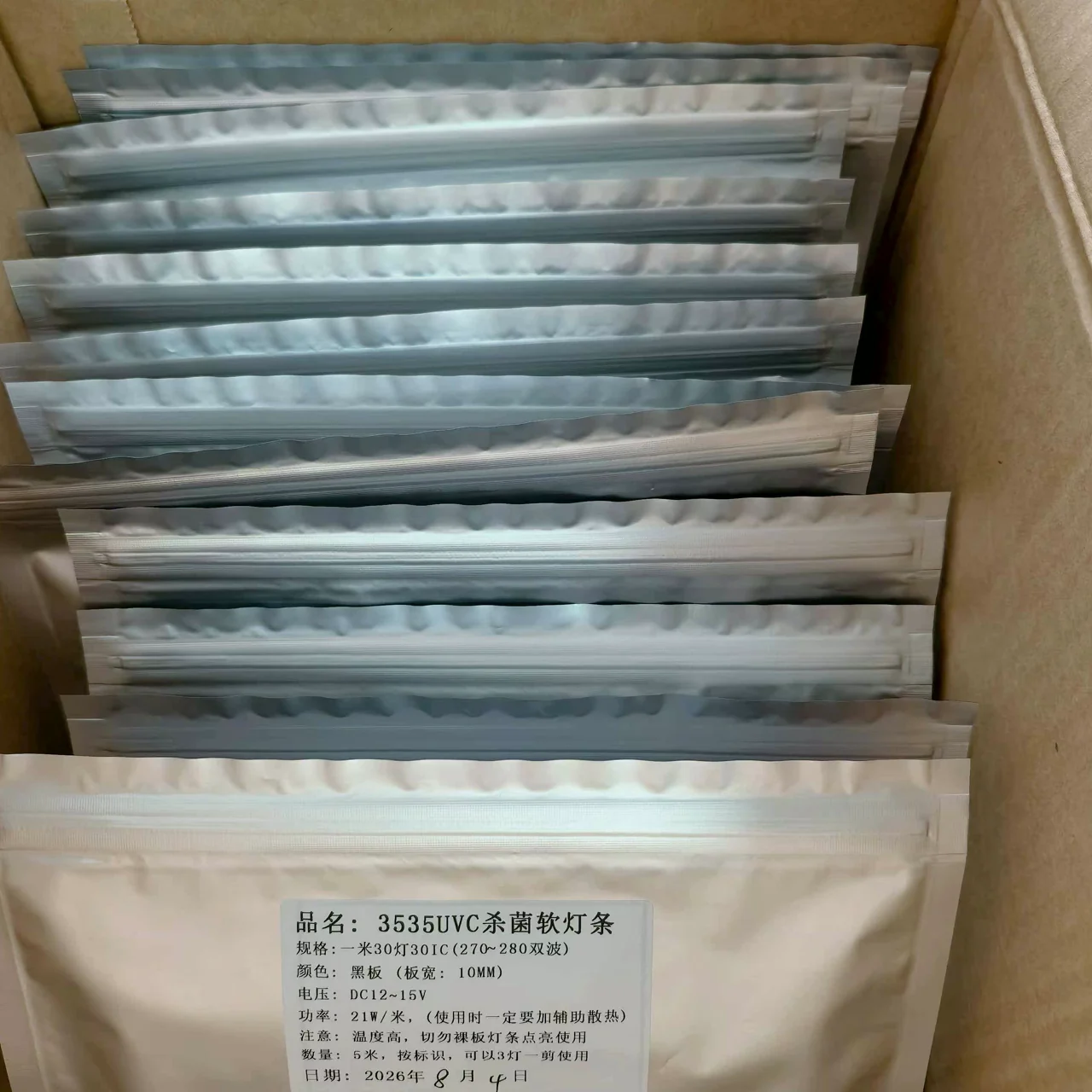 Individually sealed silver packages containing flexible UVC LED strip reels inside a carton